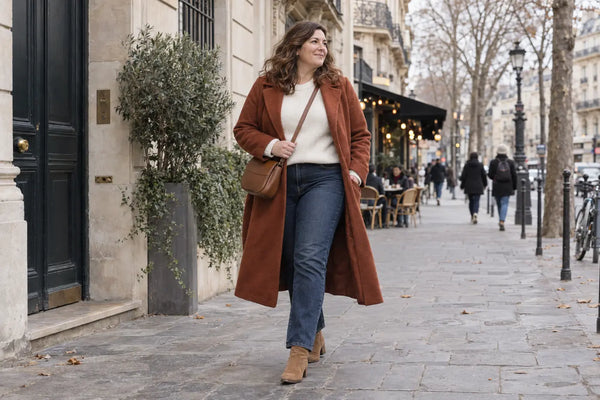 Femme ronde en jean, pull crème et manteau terracotta pour un look d’hiver