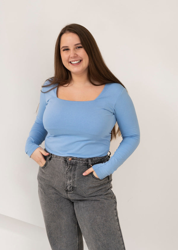 Une femme petite et ronde souriante qui porte un jean et un haut bleu clair